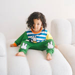 Bambino che indossa il completo da casa in bambù Miffy della linea Move, composto da felpa con motivo di bicicletta e pantaloni da jogging verdi