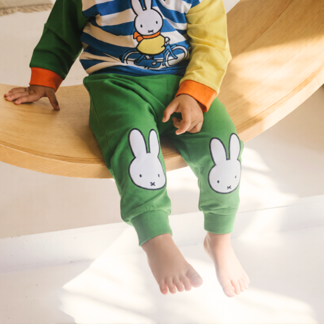 Bambino che indossa il completo da casa in bambù Miffy della linea Move, composto da felpa con motivo di bicicletta e pantaloni da jogging verdi