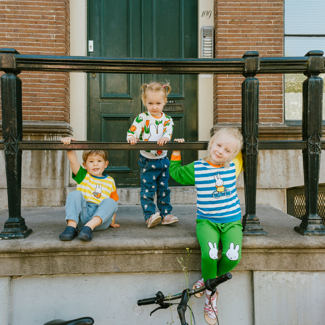 Bambino che indossa il completo da casa in bambù Miffy della linea Move, composto da felpa con motivo di bicicletta e pantaloni da jogging verdi