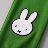 Dettaglio di design del modello Miffy del set da salotto in bambù "Move", con felpa con motivo di bicicletta e pantaloni da jogging verdi
